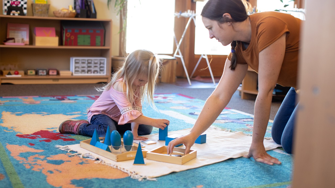 Little girl using Montessori blocks and instructor watching.